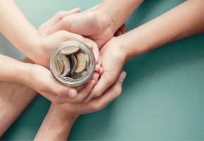 child and parent hands holding money jar