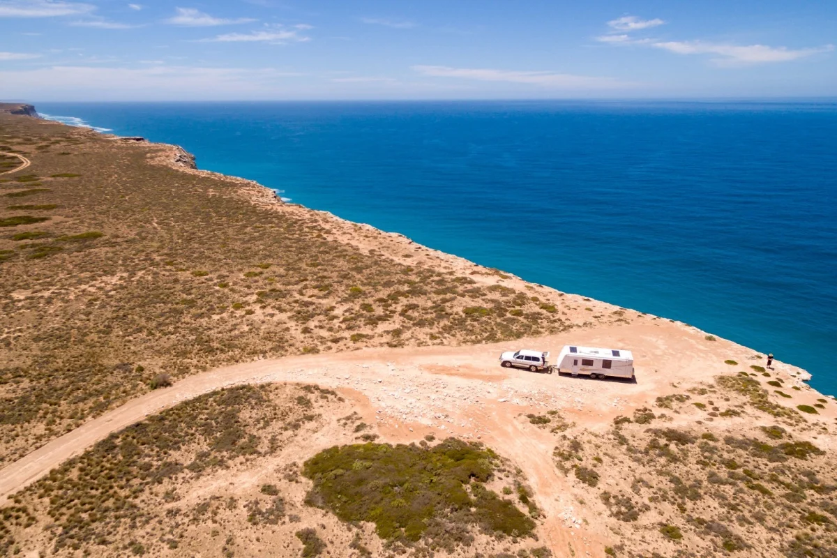 Aerial view of 4WD vehicle driving along sandy beach track near ocean